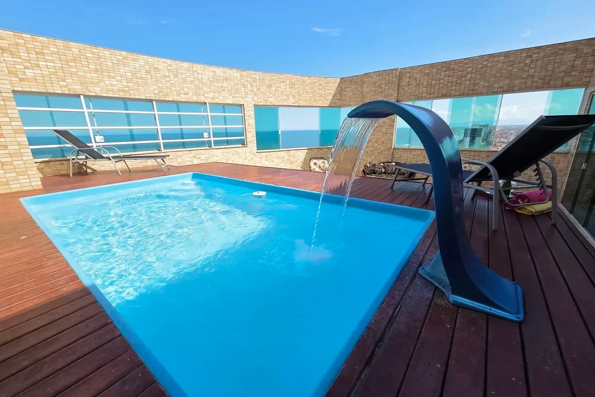 Piscina privativa com cascata no deck de madeira da cobertura, mar no horizonte